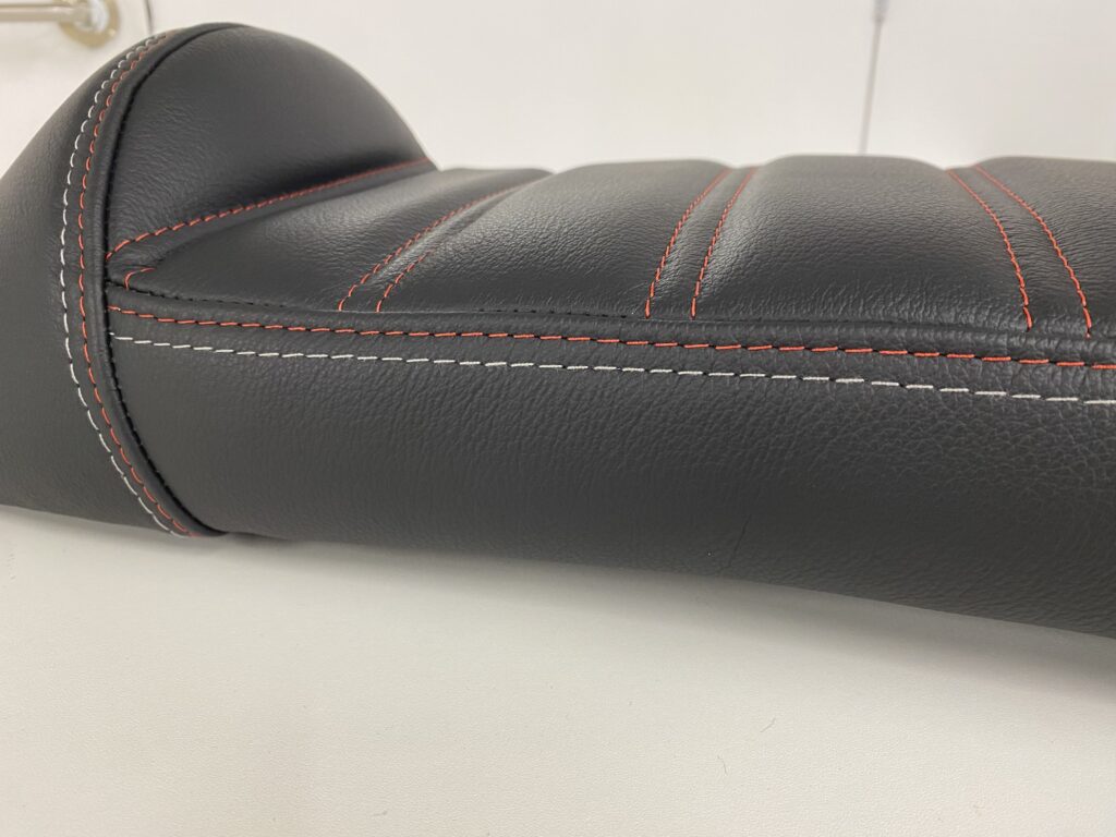 A Lambretta style, long bike seat, black in colour with fresh red stitching.